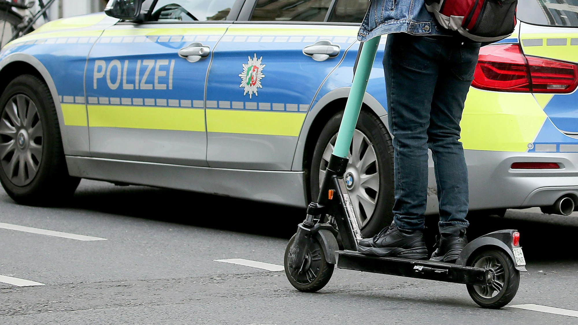 Ein Mann fährt mit einem E-Scooter an einem Polizeiauto vorbei.