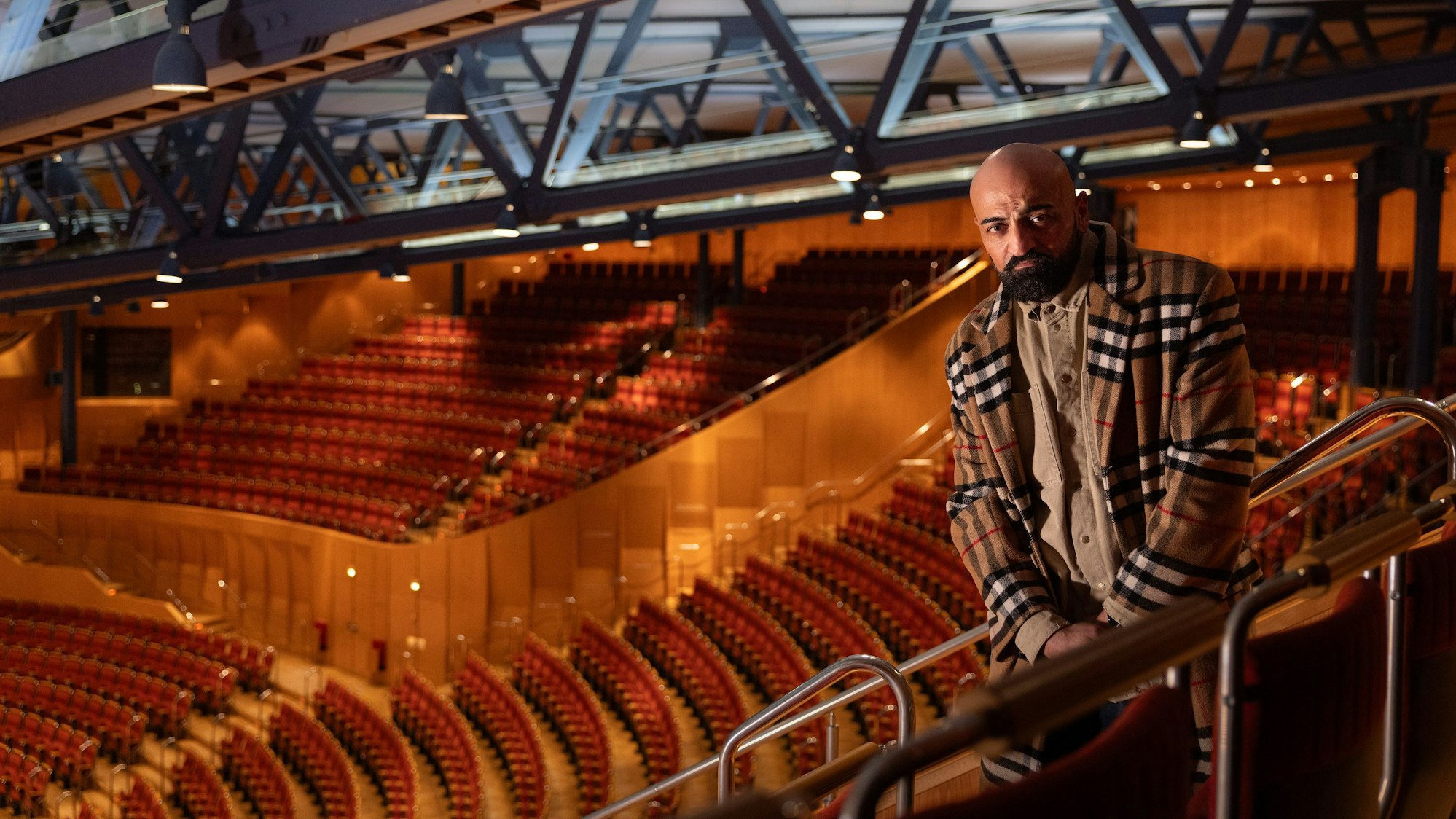 Xatar steht im leeren Zuschauerraum der Kölner Philharmonie. Er trägt ein helles kariertes Jackett.