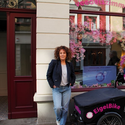 Eine Frau mit gelocktem Haar und ein Mann mit grauem Haar stehen neben einem Lastenrad mit der Aufschrift EigelBike.
