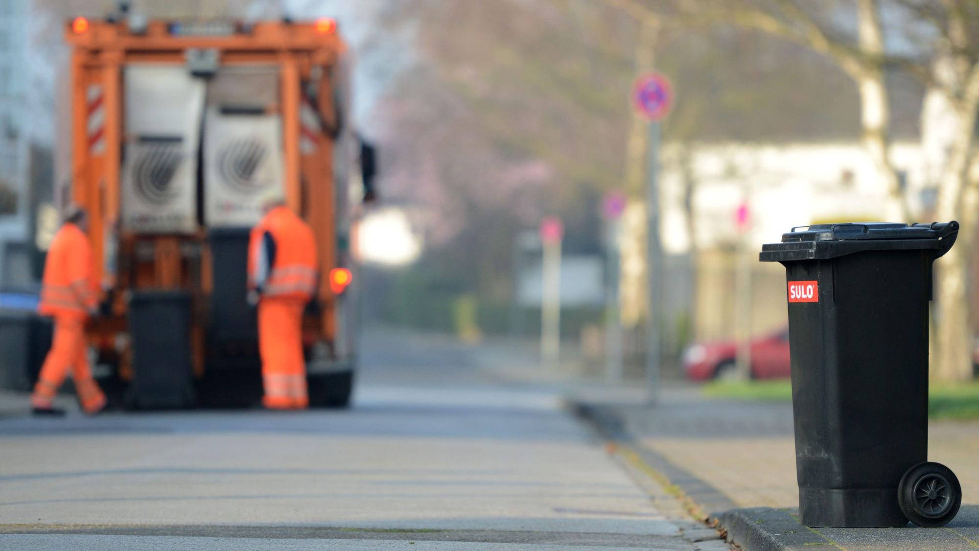 Zwei Männer von der Müllabfuhr entleeren Graue Tonnen (Symbolfoto).
