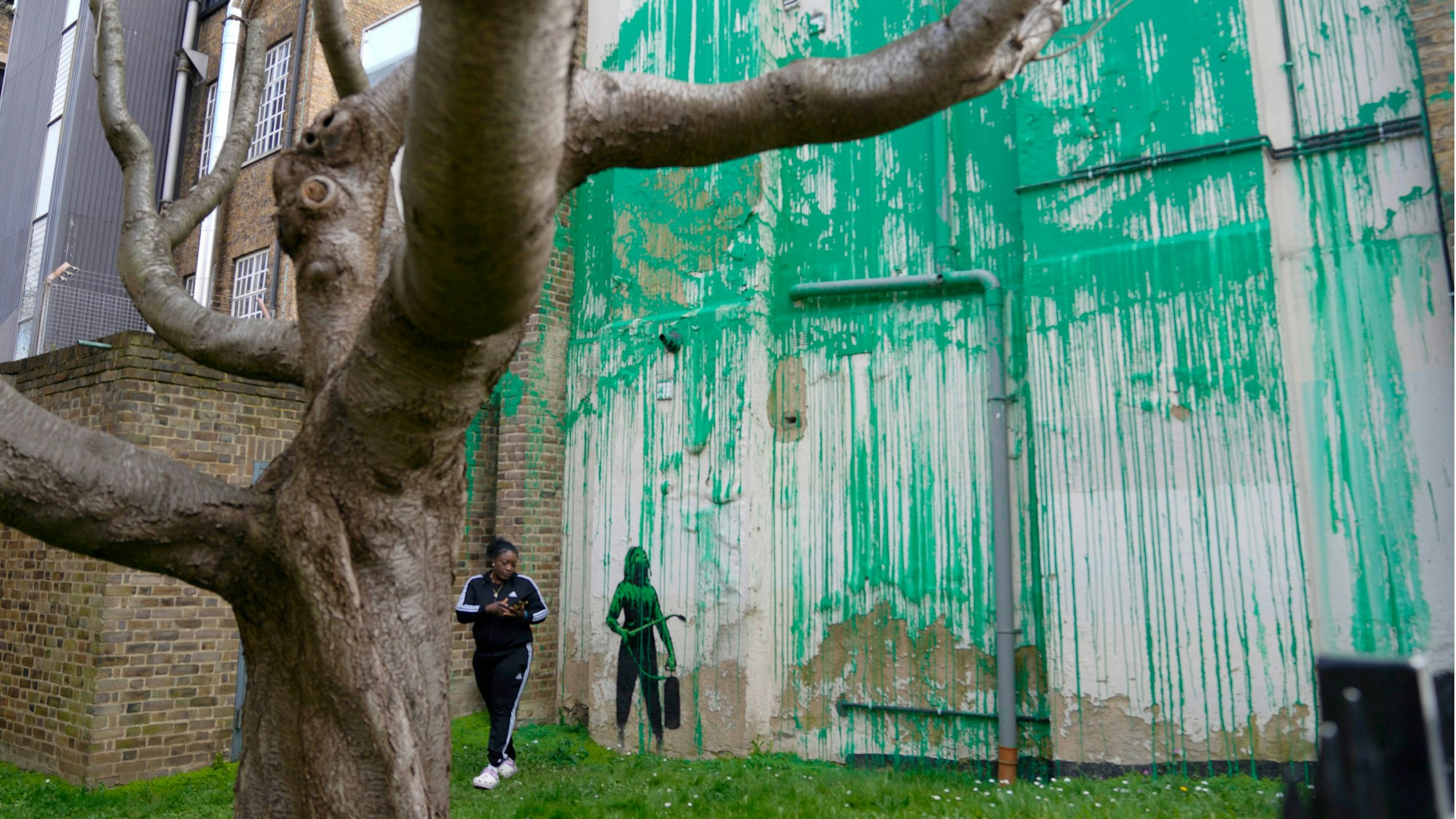 Eine Frau im Trainingsanzug steht auf einem Garten neben einer Wand, die mit Kunst besprüht wurde.