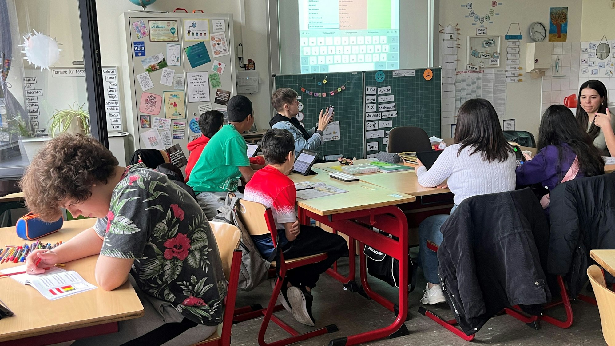 Kinder sitzen in einer Schule an Tischen, vor ihnen liegen aufgeklappte Hefte.
