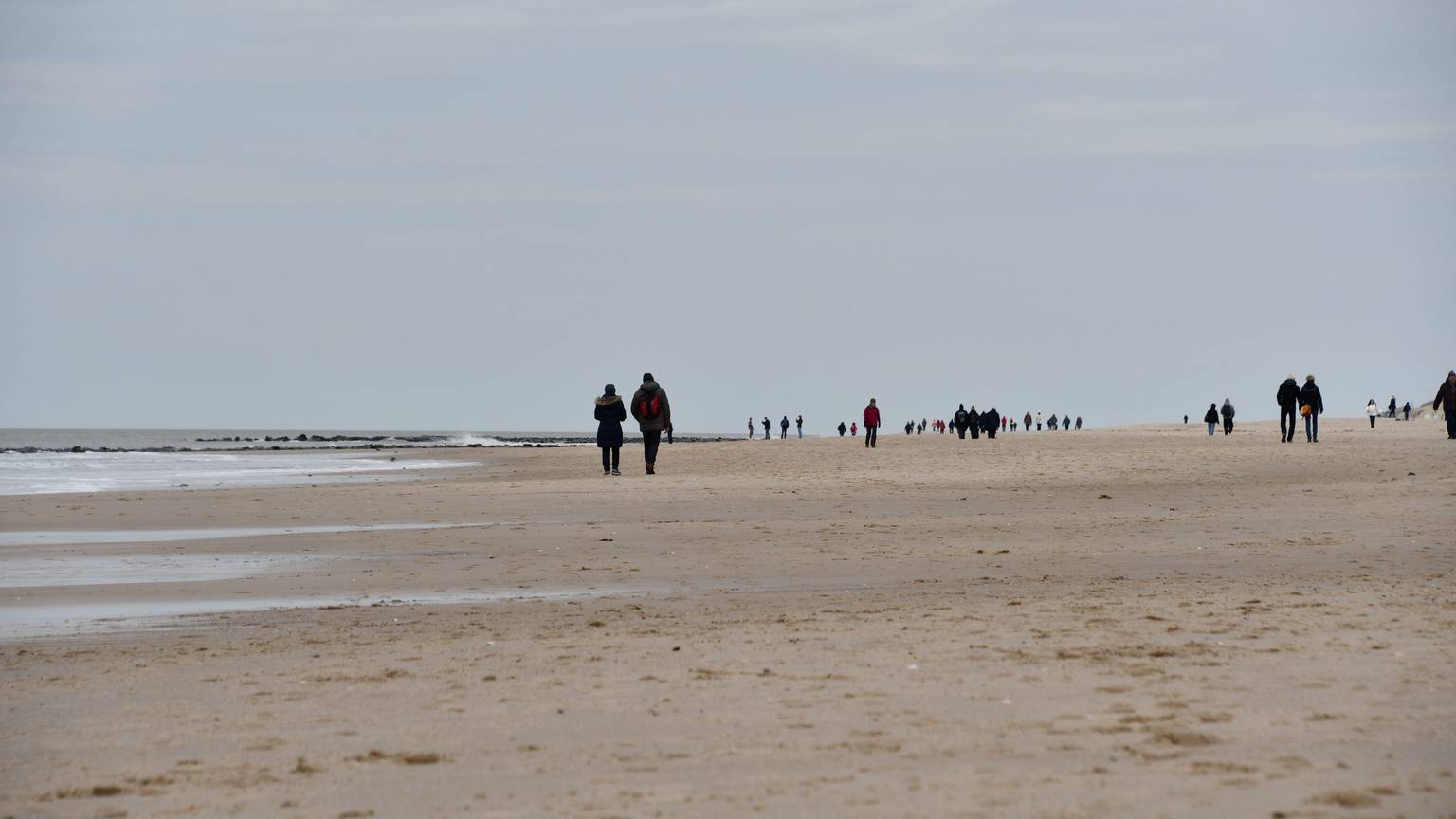 Spaziergänger sind am Montag bei bedecktem Himmel am Strand von Westerland unterwegs.