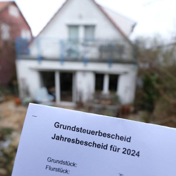 Ein Grundsteuerbescheid für 2024 wird vor einem Privatgrundstück hochgehalten. Für die neue Berechnung der Grundsteuer müssen bundesweit fast 36 Millionen Grundstücke neu bewertet werden.