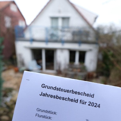Ein Grundsteuerbescheid für 2024 wird vor einem Privatgrundstück hochgehalten. Für die neue Berechnung der Grundsteuer müssen bundesweit fast 36 Millionen Grundstücke neu bewertet werden.