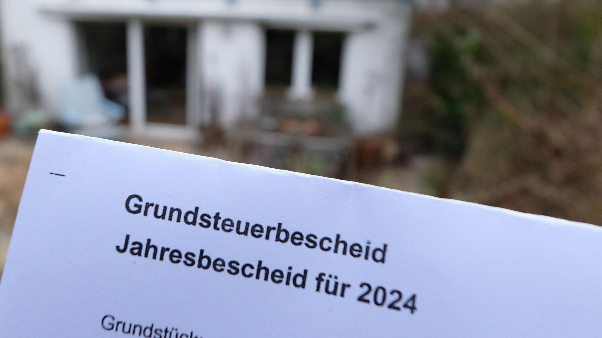Ein Grundsteuerbescheid für 2024 wird vor einem Privatgrundstück hochgehalten. Für die neue Berechnung der Grundsteuer müssen bundesweit fast 36 Millionen Grundstücke neu bewertet werden.