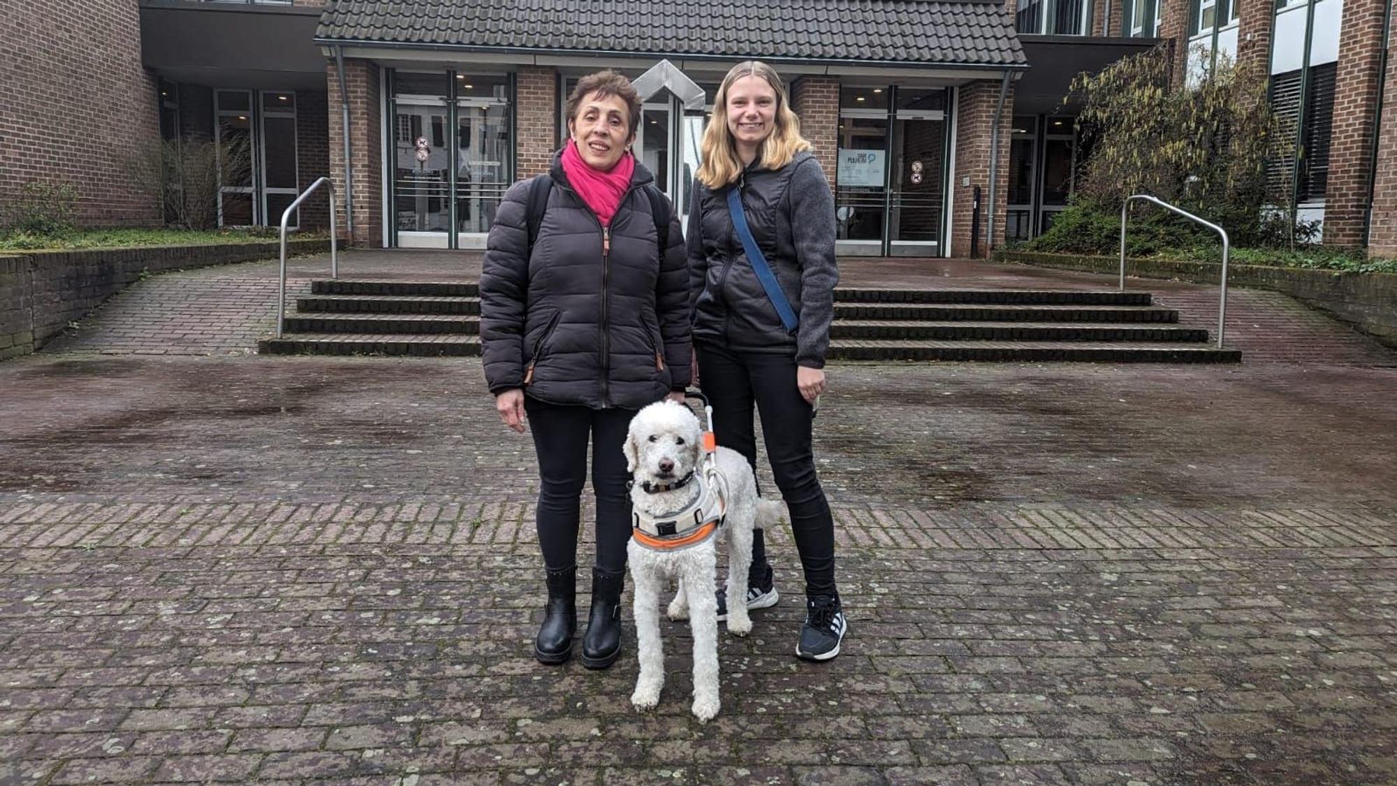 Zu sehen sind zwei Frauen, die ältere ist blind, immer an ihrer Seite ist ihr Blindenführhund Rainer.