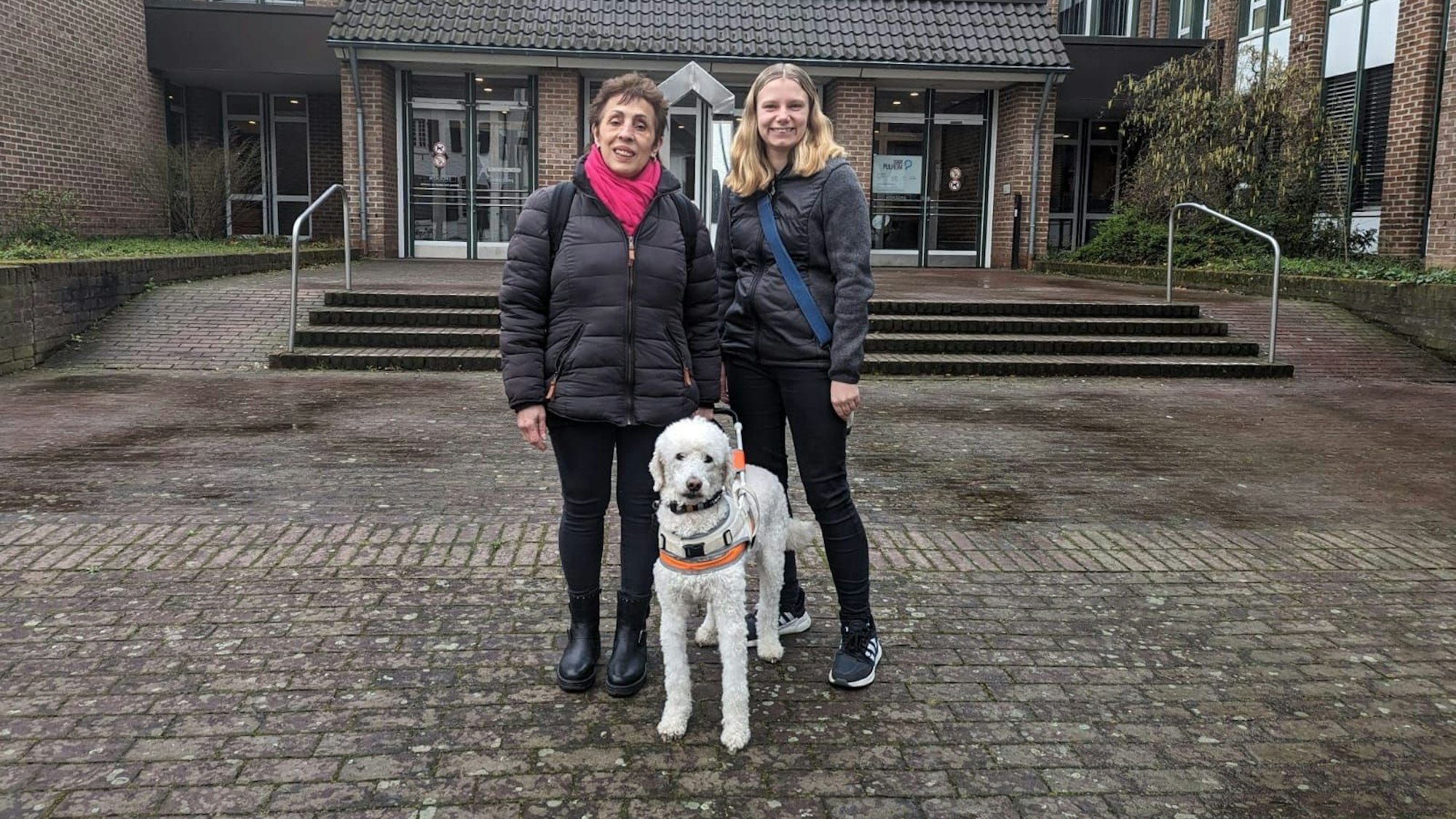 Zu sehen sind zwei Frauen, die ältere ist blind, immer an ihrer Seite ist ihr Blindenführhund Rainer.