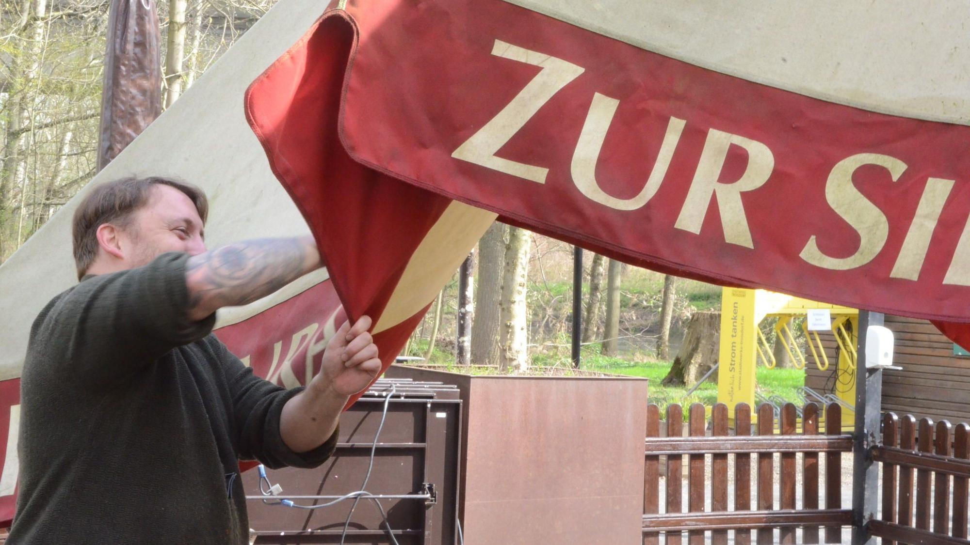 Ein Mann säubert einen großen Sonnenschirm eines Biergartens.