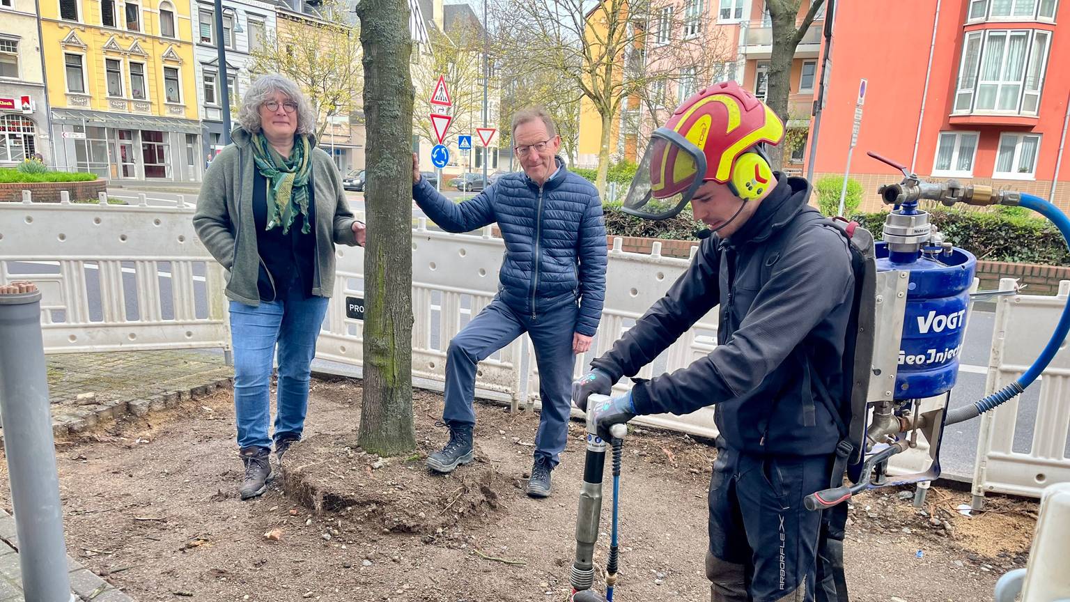 Ein Mitarbeiter einer Fachfirma pumpt Luft in die Erde, im Hintergrund Andrea Sahm und Ulrich Hammer vom Stadtgrün.