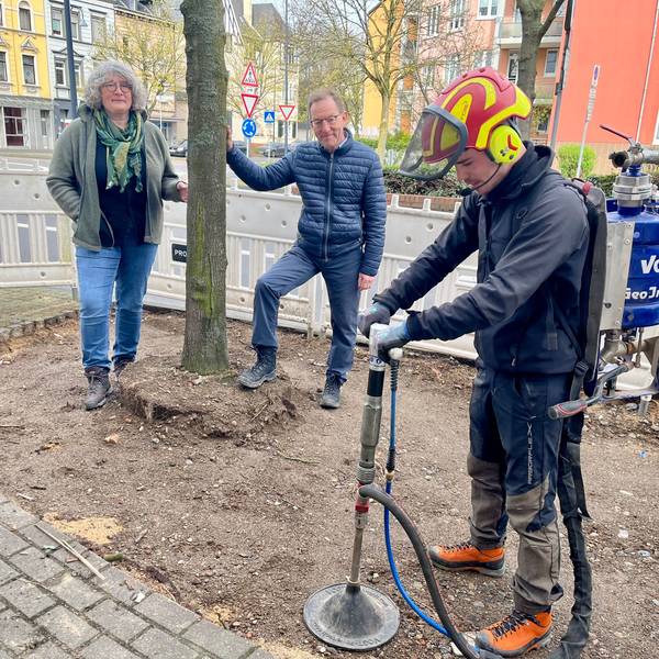Ein Mitarbeiter einer Fachfirma pumpt Luft in die Erde, im Hintergrund Andrea Sahm und Ulrich Hammer vom Stadtgrün.
