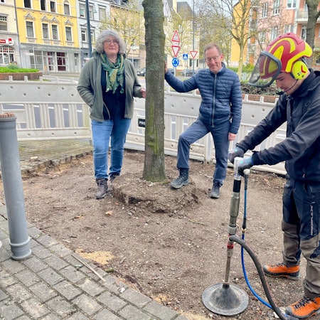 Ein Mitarbeiter einer Fachfirma pumpt Luft in die Erde, im Hintergrund Andrea Sahm und Ulrich Hammer vom Stadtgrün.