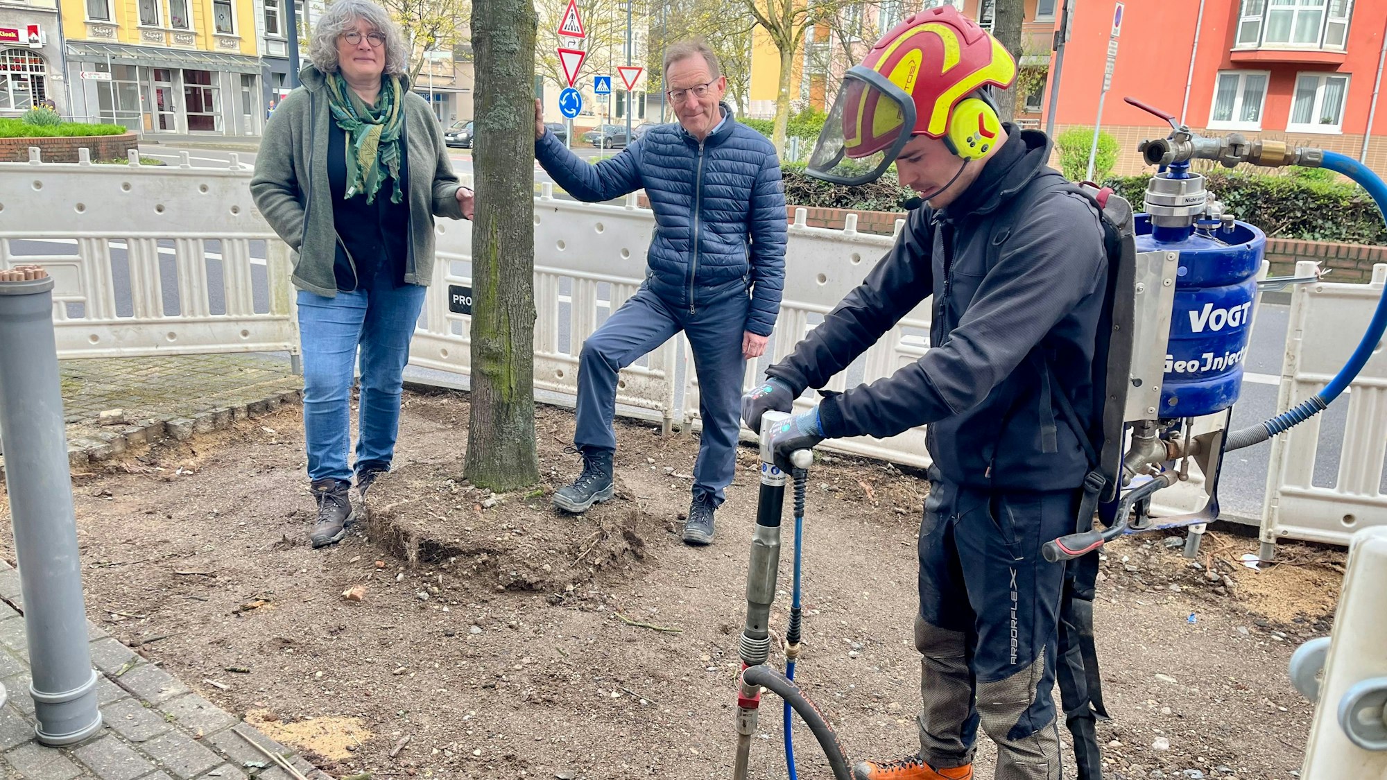 Ein Mitarbeiter einer Fachfirma pumpt Luft in die Erde, im Hintergrund Andrea Sahm und Ulrich Hammer vom Stadtgrün.