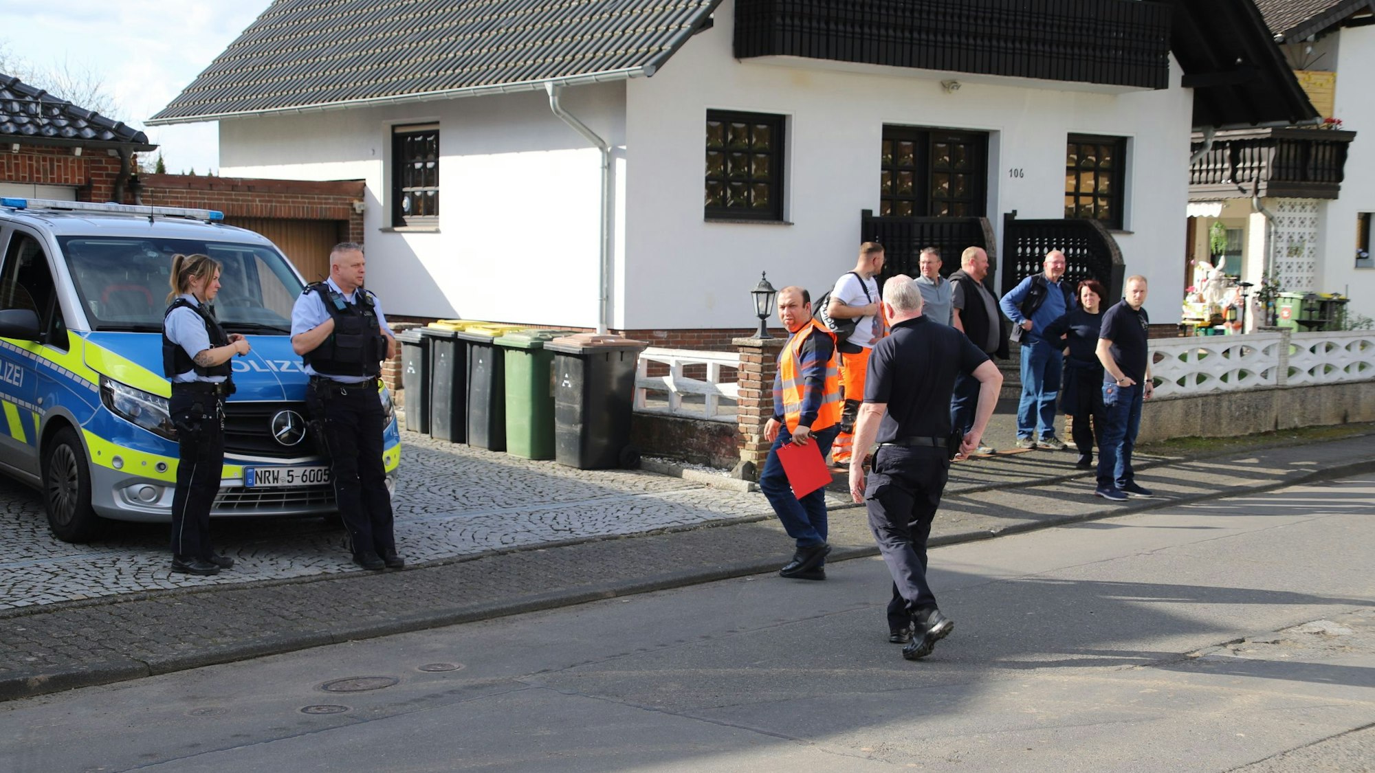 Menschen stehen vor einem Haus, ein Polizeiauto steht daneben.