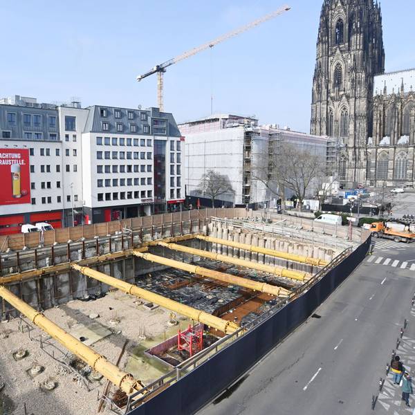 Das Bild zeigt eine Baustellengrube vor einigen Gebäuden, im Hintergrund ist der Dom zu sehen.