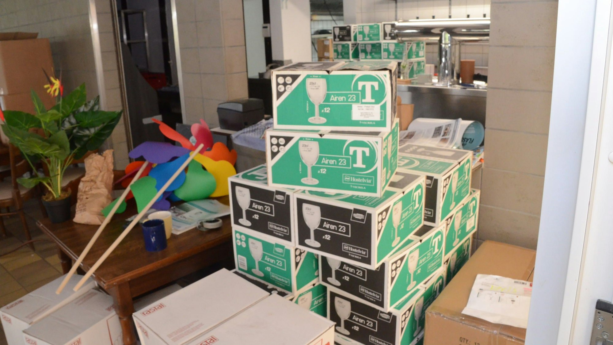 Blick in den Innenraum eines Lokals. Auf einem Tisch stapeln sich Kartons mit Weingläsern, im Hintergrund ist ein Schanktresen zu erkennen.