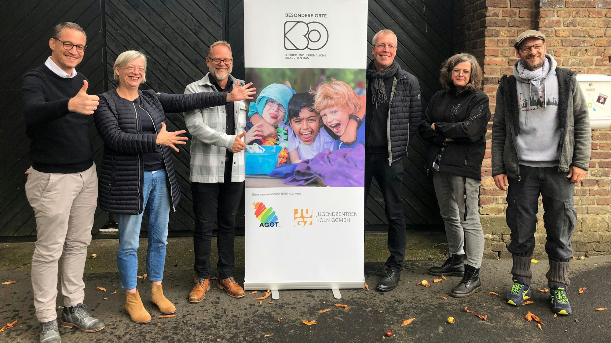 Sechs Menschen stehen links und rechts von einem Plakat, das auf Jugendzentren aufmerksam macht.