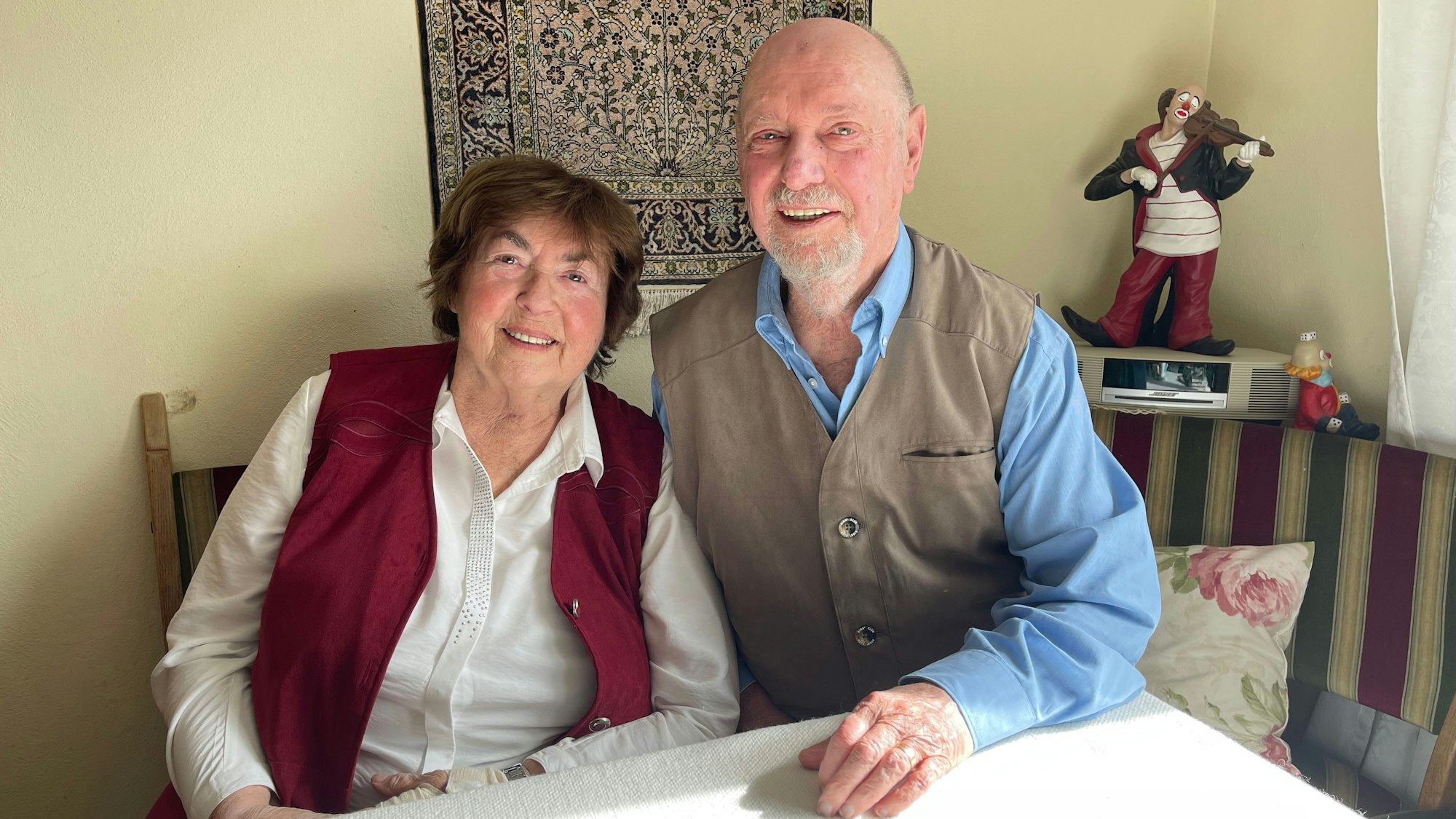 Die Eheleute sitzen an einem Tisch und lächeln.