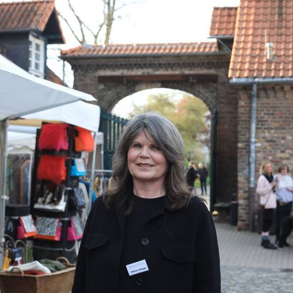 Eine Frau steht im Hof eines großen Gutshofs, links neben ihr ist ein Verkaufsstand zu sehen.