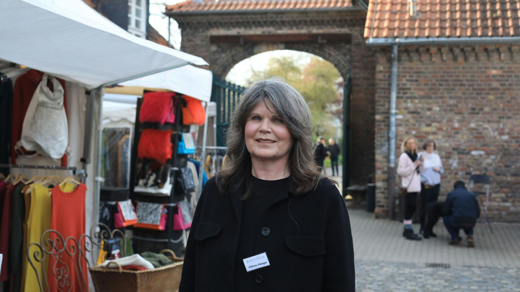 Eine Frau steht im Hof eines großen Gutshofs, links neben ihr ist ein Verkaufsstand zu sehen.