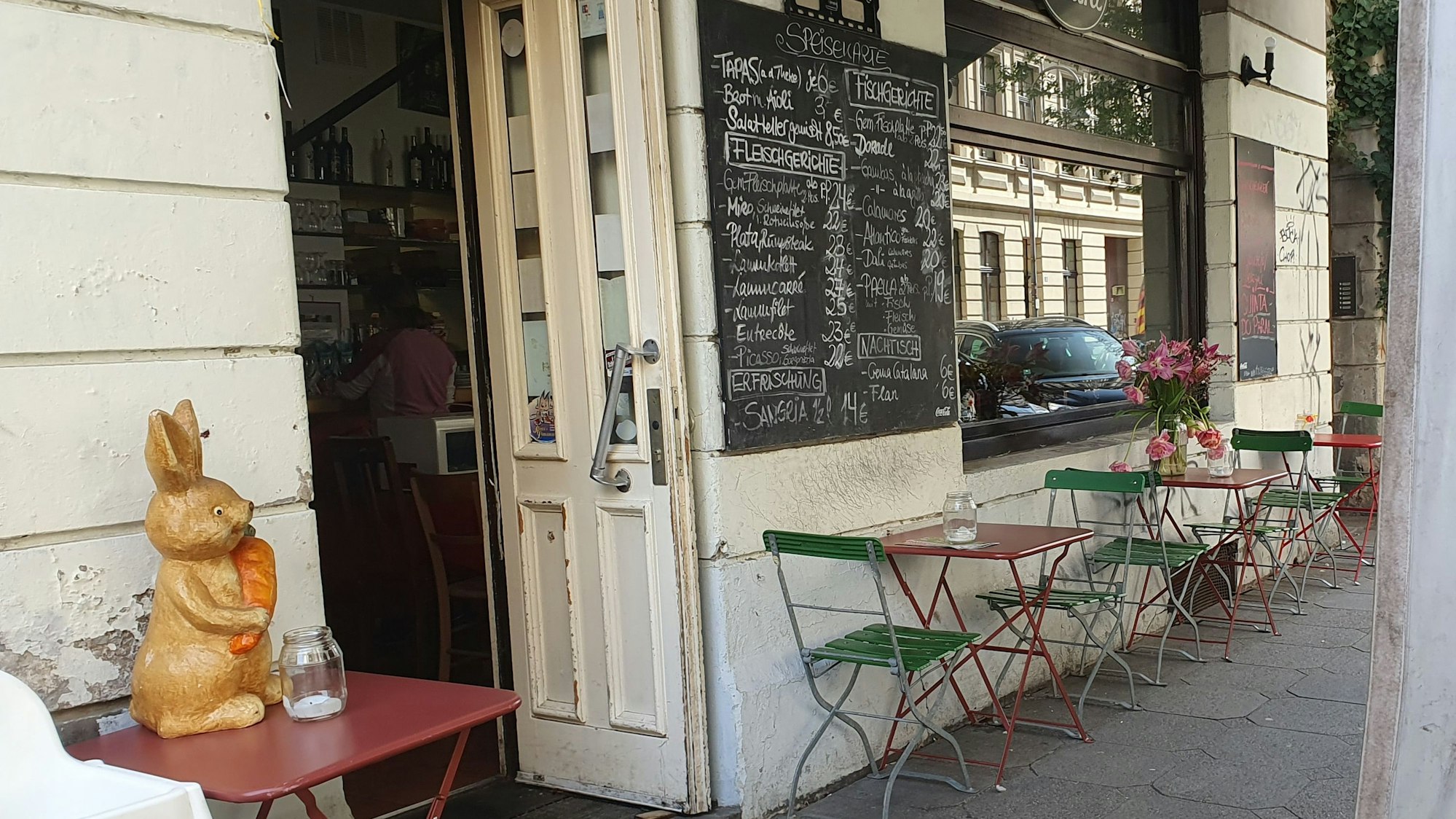 Außenbereich eines Restaurants, bunte Tische und Stühlen, auf einem der Tische steht eine Osterhasen-Statue