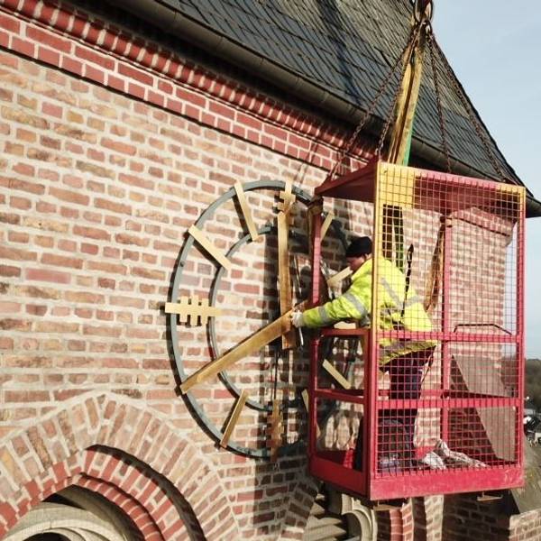 Zu sehen ist ein Arbeiter, der die goldene Kirchturmuhr repariert.