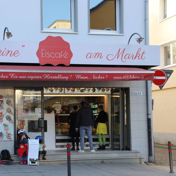 Das kleine Eiscafe am Markt in Eitorf in der Außenansicht. Menschen bestellen an der Eistheke, links im Bild ist ein Fahrrad mit Kindersitz an die Hauswand gelehnt.