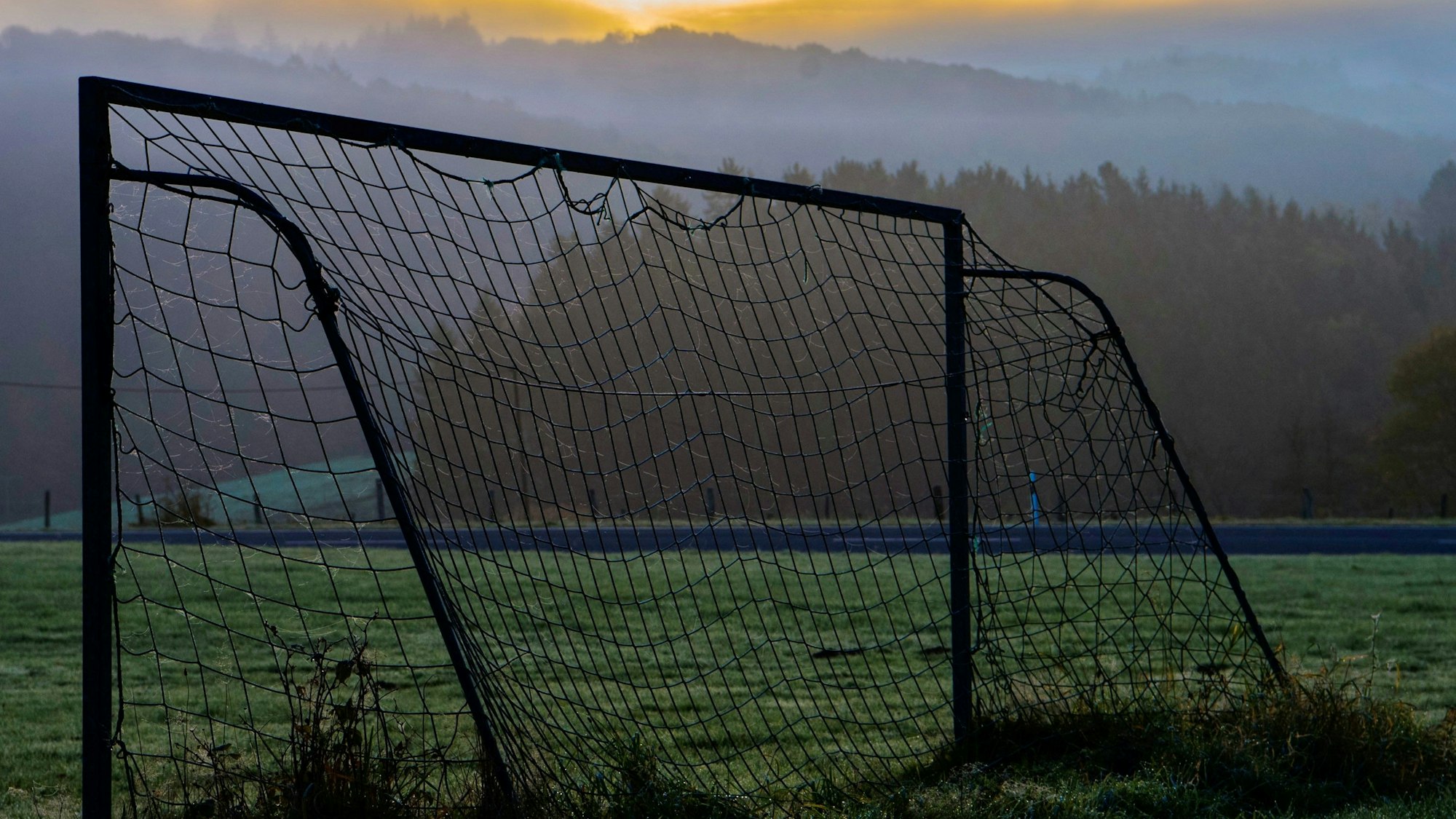 Das Bild zeigt den Bolzplatz zwischen Kolvenbach und Bouderath. Im Hintergrund geht die Sonne auf.