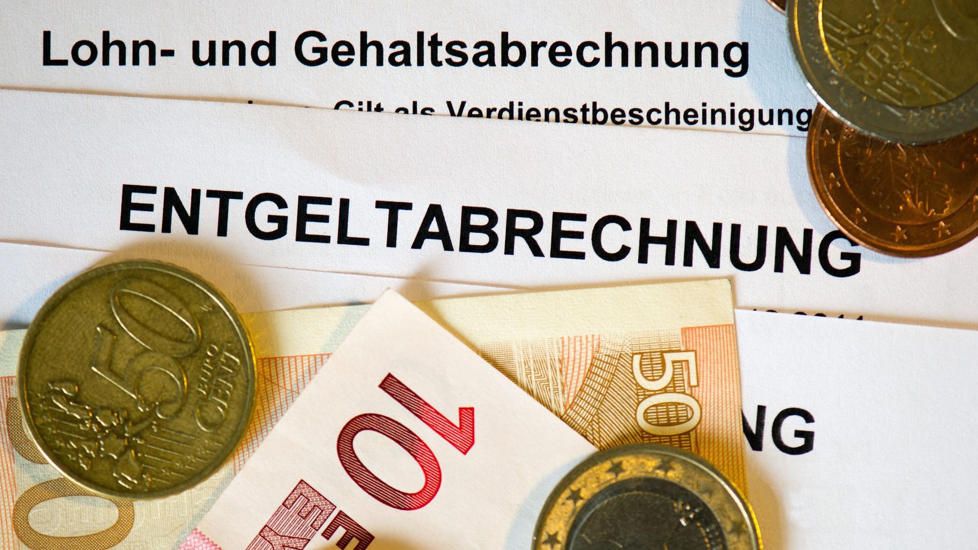 Auf Lohn- und Gehaltsabrechnungen (Entgeltabrechnungen) liegen Euromünzen und Eurogeldscheine.