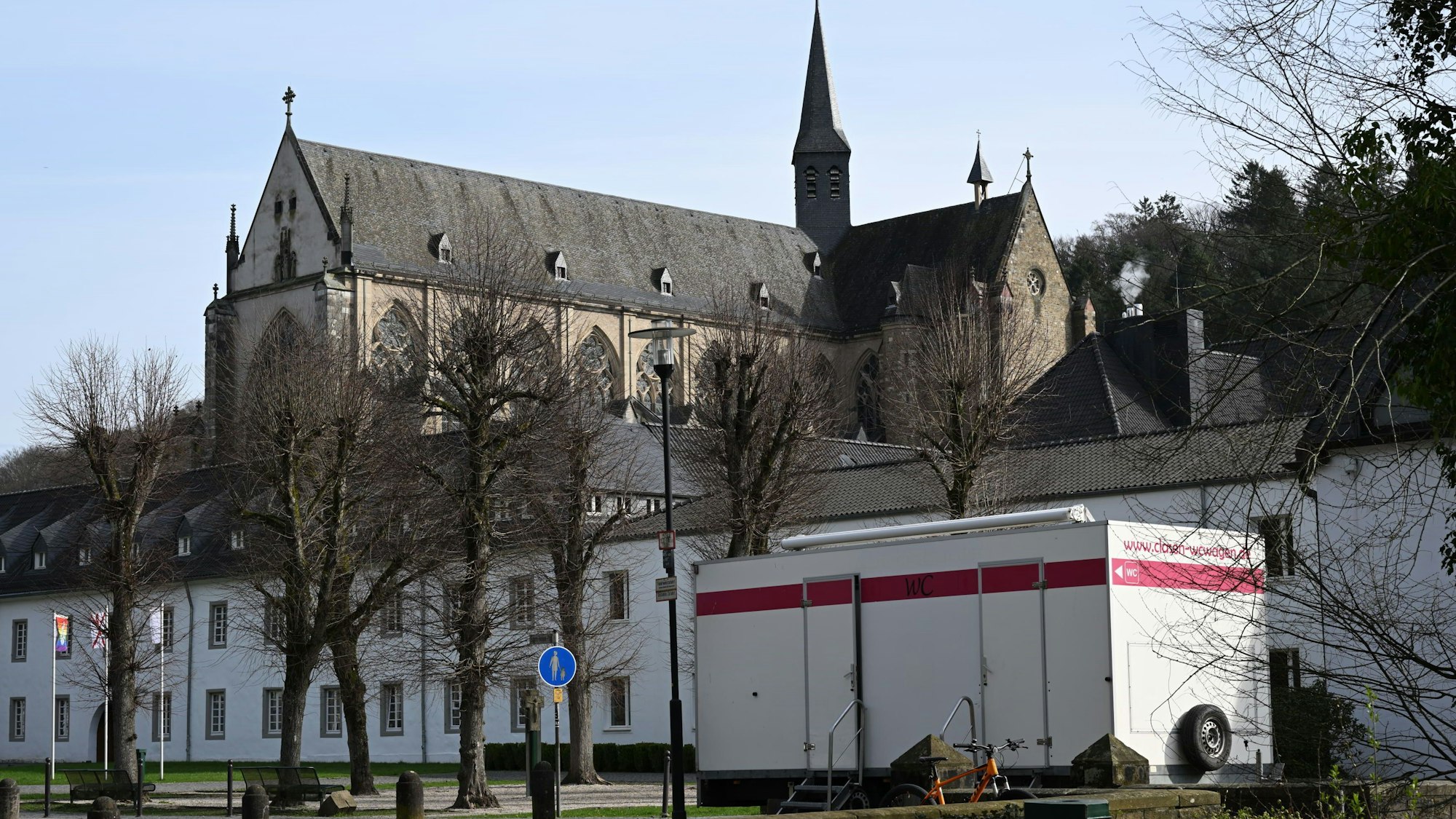 Ein mobiler Toilettenwagen steht vor der Jugendbildungsstätte Haus Altenberg. Im Hintergrund der Altenberger Dom.