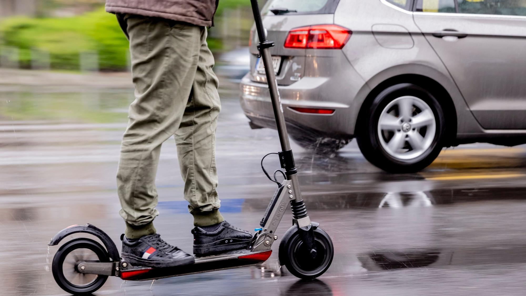 Auf dem Foto sind ein E-Scooterfahrer und ein Auto zu sehen.