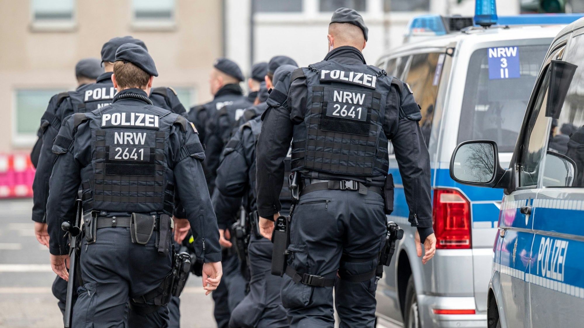 Polizeikräfte im Einsatz in voller Montur. Neben ihnen stehen aufgereiht mehrere Polizeiwagen.