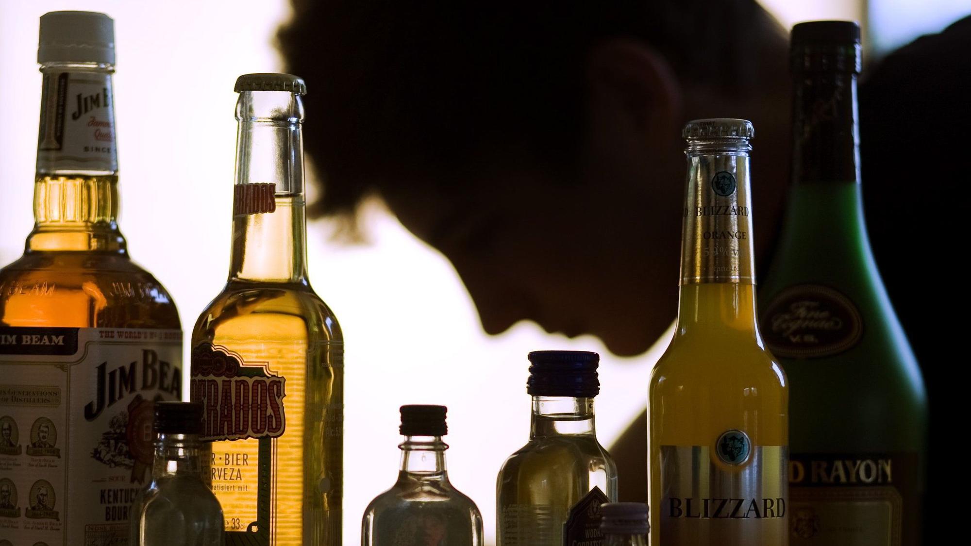 ARCHIV - ILLUSTRATION - Ein Jugendlicher sitzt hinter Flaschen mit Alkohol.