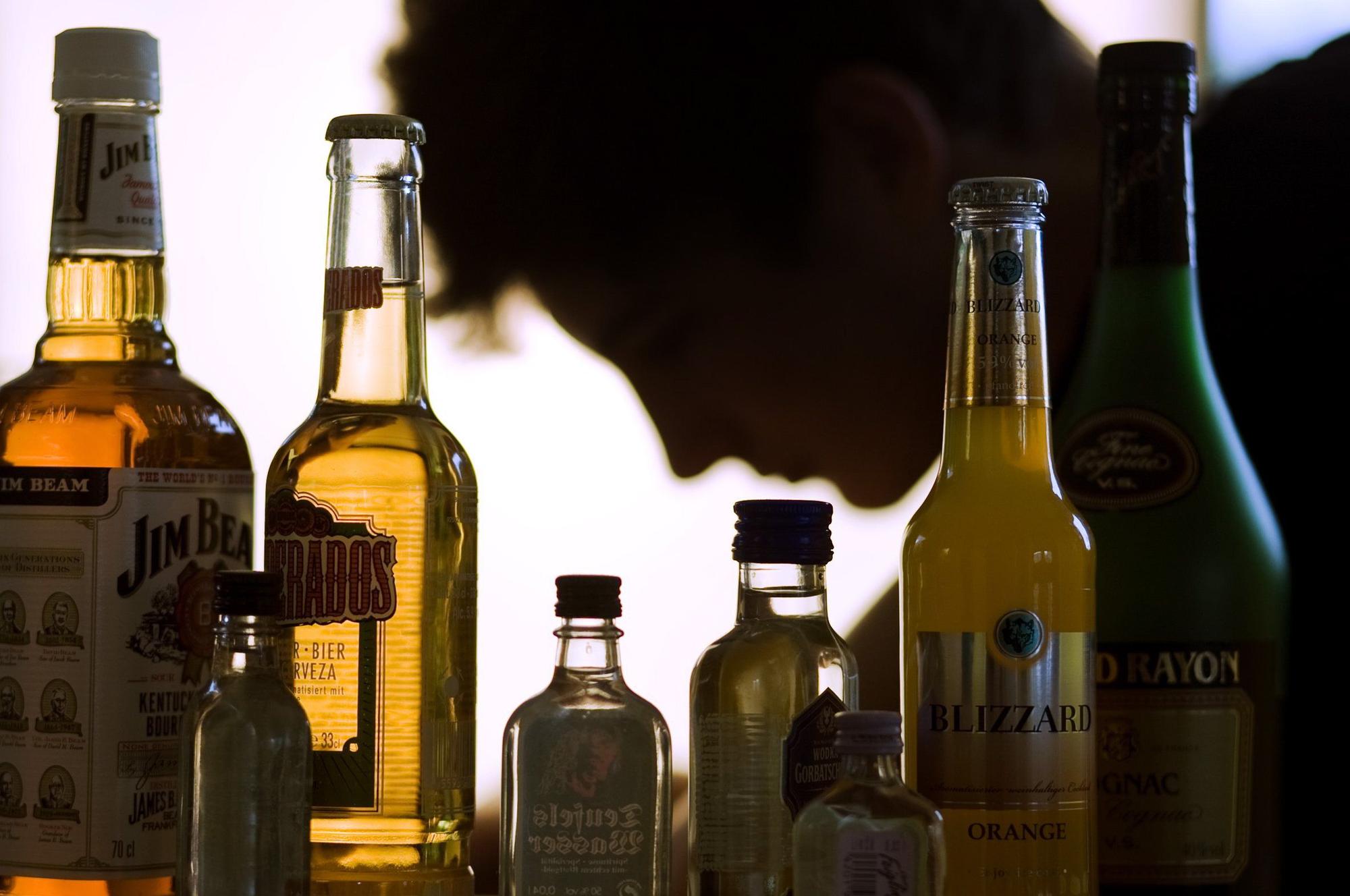 Ein Jugendlicher sitzt hinter Flaschen mit Alkohol,