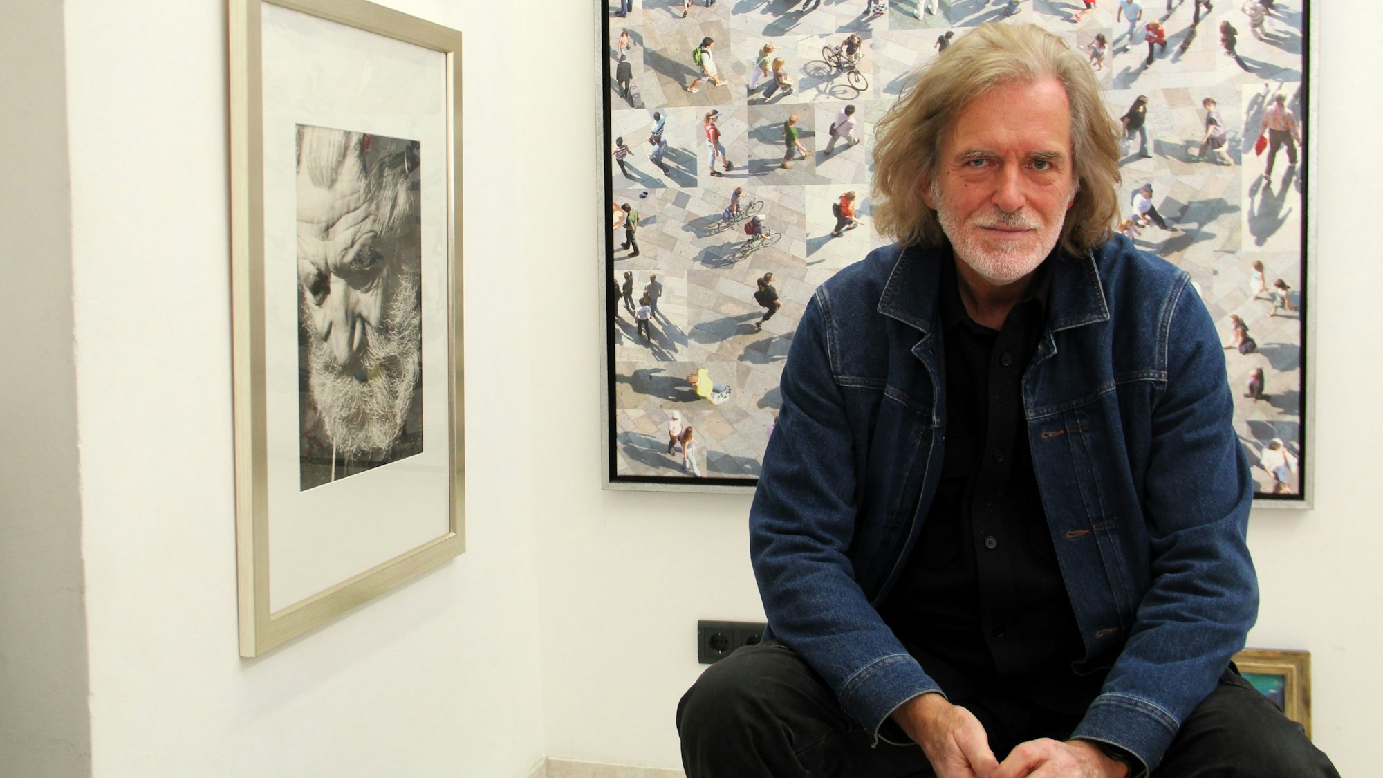 Ein Mann sitzt vor verschiedenen Gemälden auf einem Hocker.