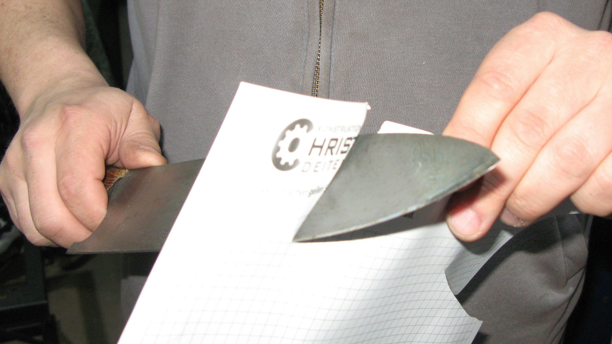 Ein Mann schneidet mit einem Damaszener in ein Blatt Papier.