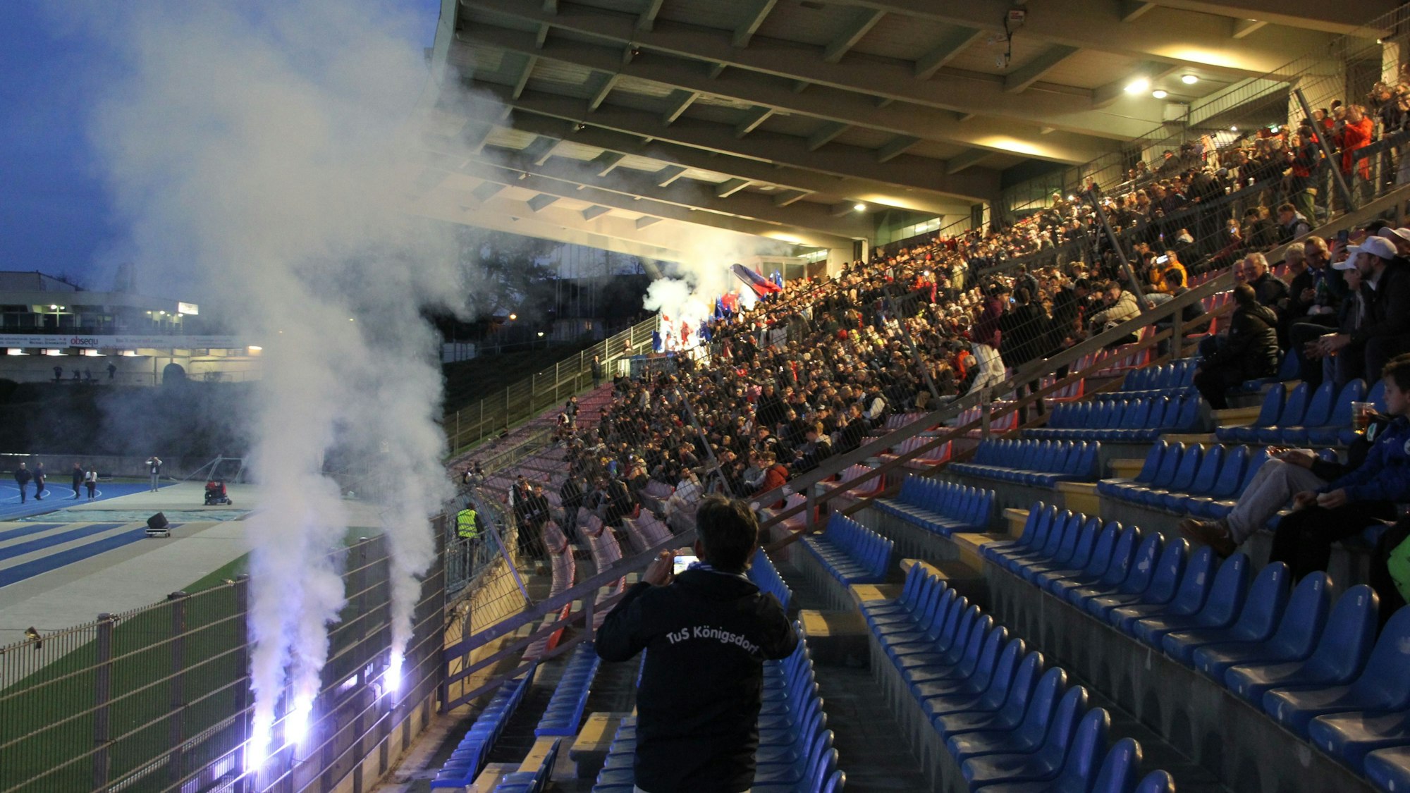 Auf der Tribüne eines Fußballstadions brennen bengalische Fackeln.