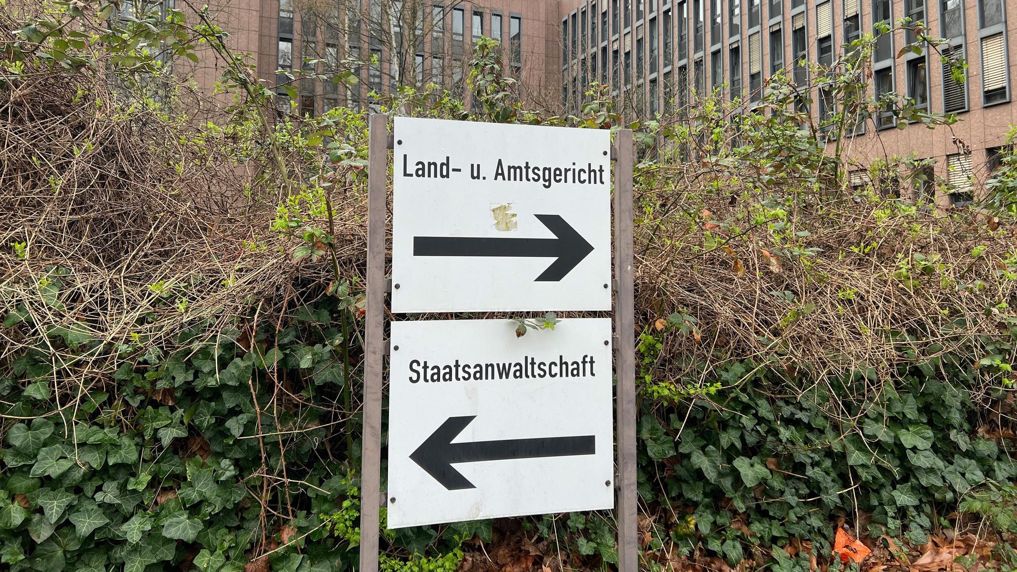 Auf dem Foto ist ein Schild vor dem Kölner Gerichtszentrum zu sehen, das auf das Land- und Amtsgericht sowie die Staatsanwaltschaft hinweist.