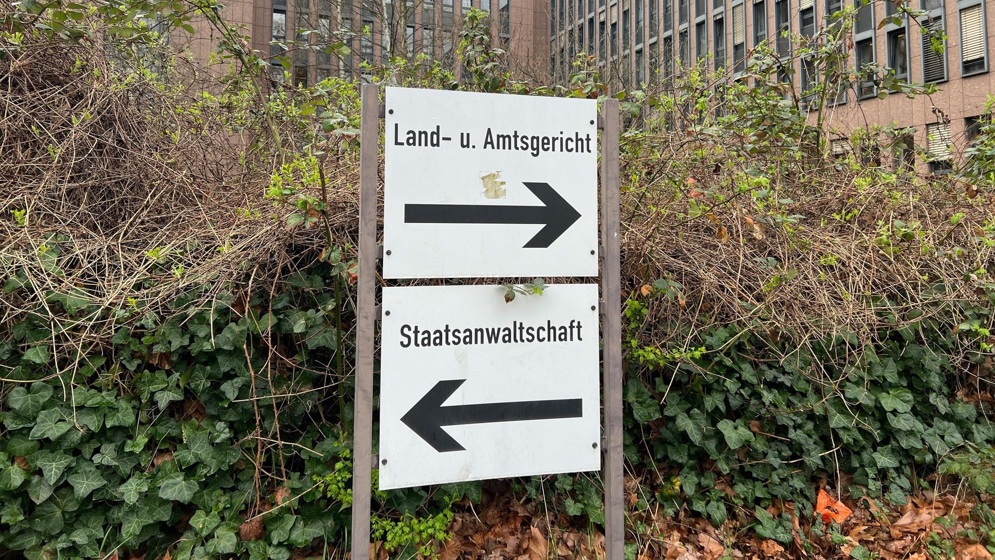 Auf dem Foto sind Schilder zu sehen,, die zum Land- und Amtsgericht Köln und zur Staatsanwaltschaft weisen. Im Hintergrund ist das Gerichtsgebäude zu suchen.
