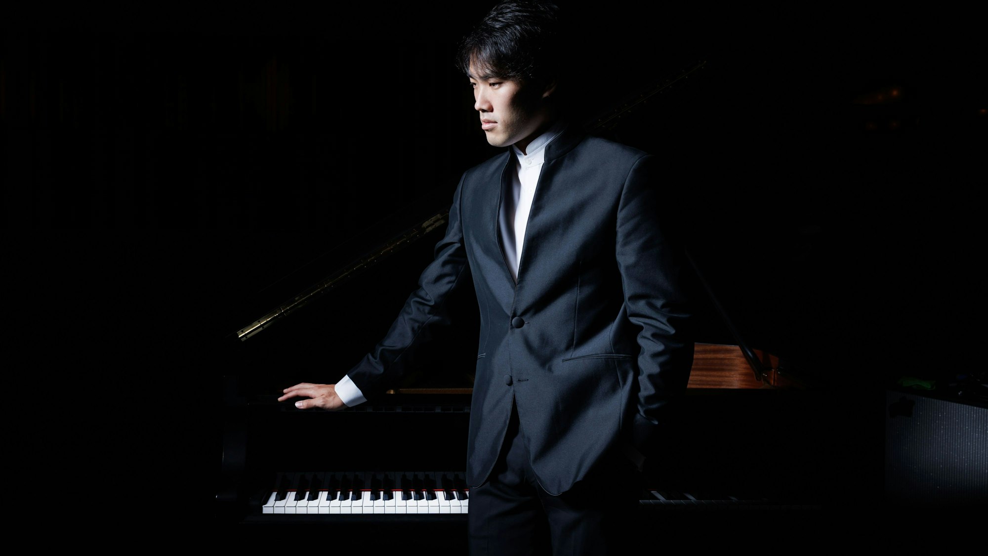 Auf dem Bildi st Bruce Liu zu sehen, der seinen ersten Blick leicht abwärts zur Seite richtet. Er trägt einen Anzug und ruht mit einer Hand auf einem Flügel, der aber wegen der Dunkelheit mit dem schwarzen Hintergrund verschmilzt.