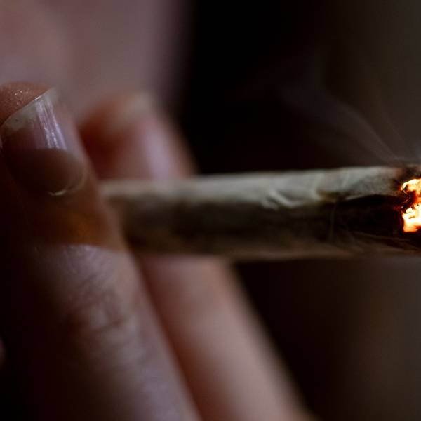 Eine Person zieht an einem Joint, den sie zwischen zwei Fingern hält.