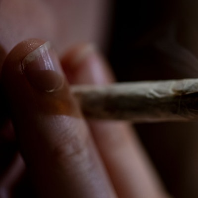 Eine Person zieht an einem Joint, den sie zwischen zwei Fingern hält.