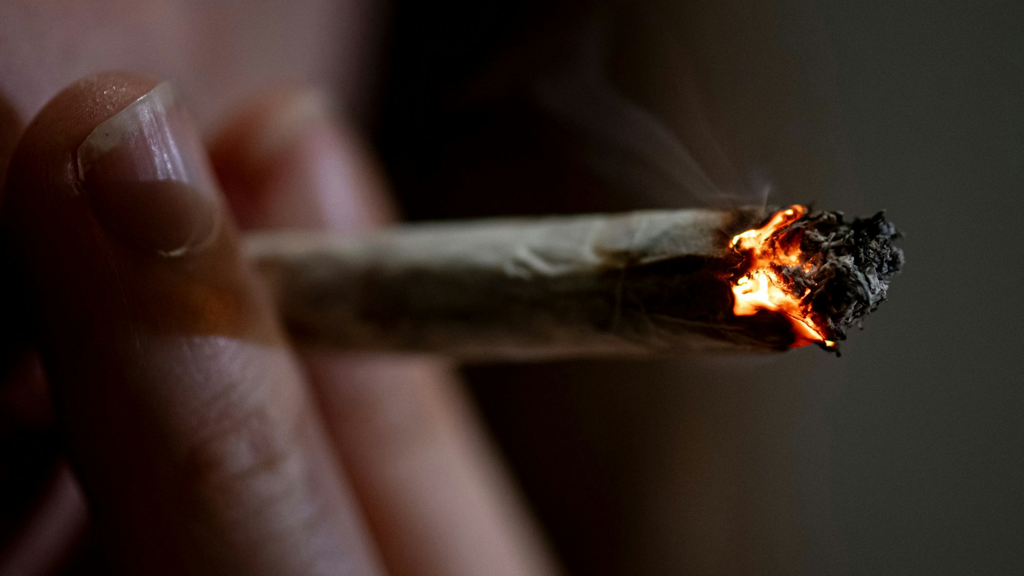 Eine Person zieht an einem Joint, den sie zwischen zwei Fingern hält.