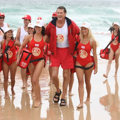 David Hasselhoff, der frühere „Baywatch“-Schauspieler und Sänger, trifft mit jungen Frauen und Männern - alle im Stil der TV-Serie „Baywatch“ gekleidet, zu einem Werbetermin am Bondi Beach ein.