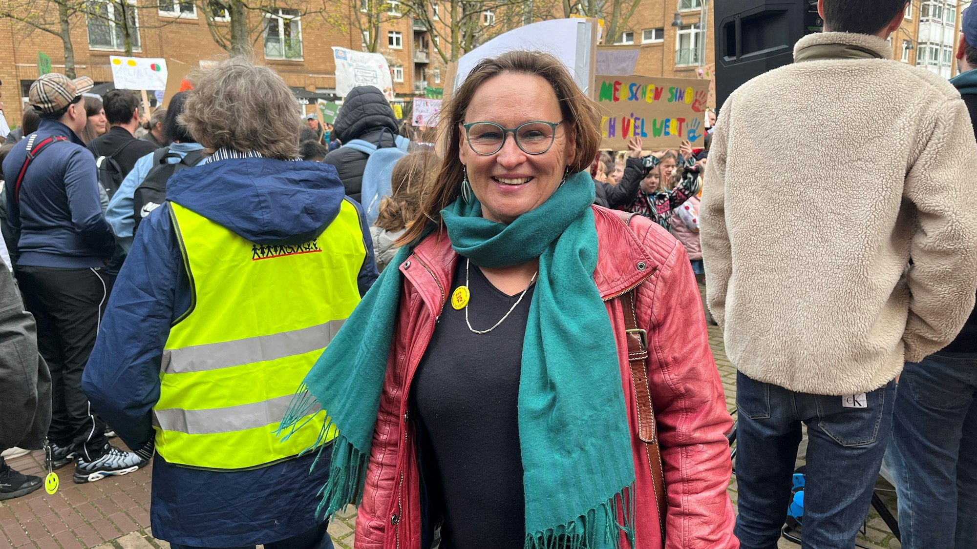 Eine Frau mit roter Jacke steht vor einer Demonstration.