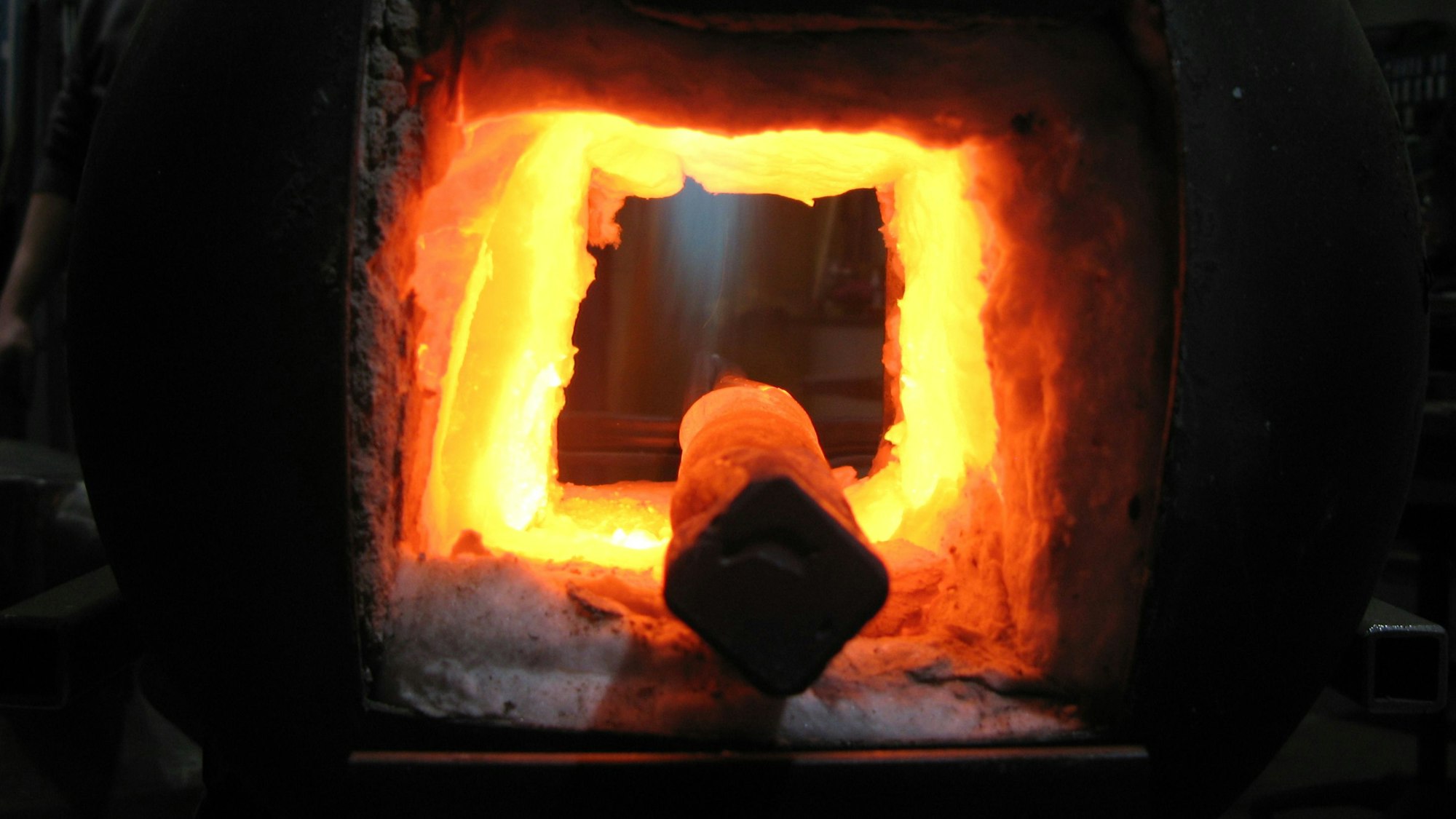 Blick in das feurig-rot-orange-gelbe Innere der Gas-Esse, in der ein glühender Stahlstab liegt.