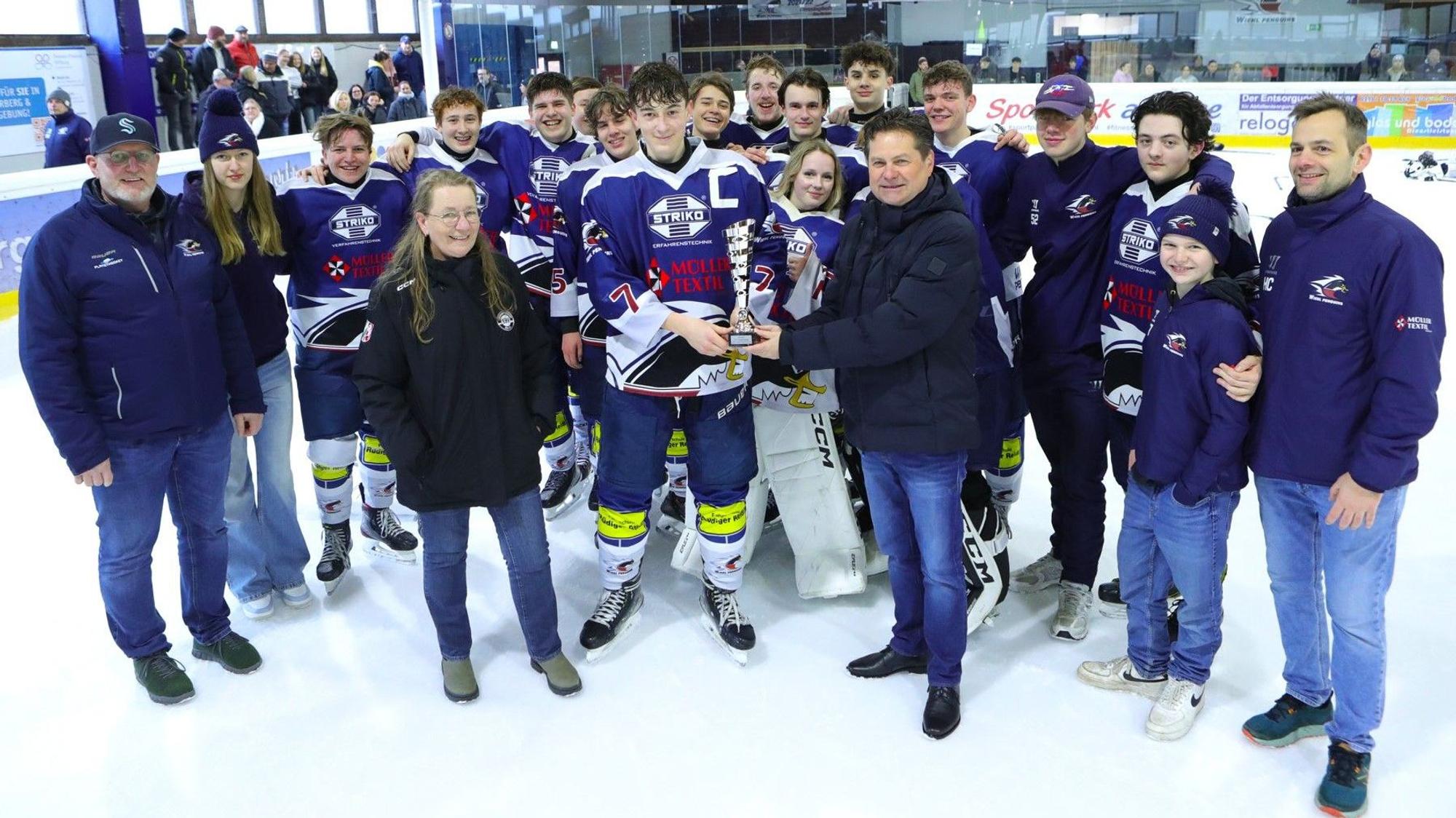 Während sich im Hintergrund die U17-Mannschaft der Wiehl Penguins aufgestellt hat, übergibt Bürgermeister Ulrich Stücker im Vordergrund den Meisterpokal an den Kapitän.