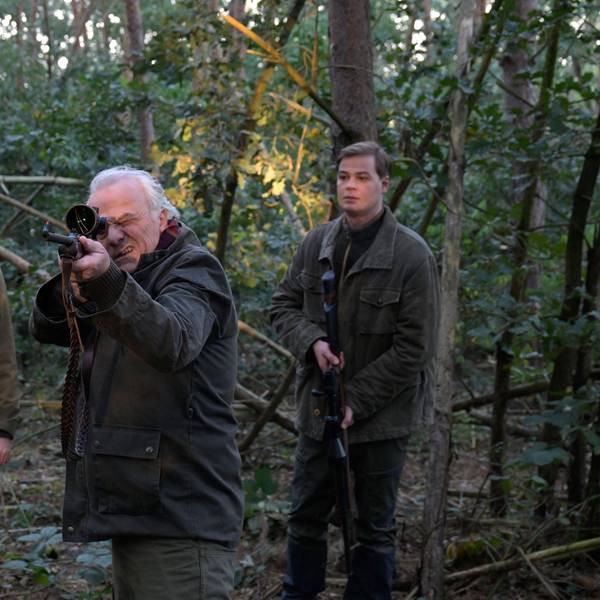Die drei Charaktere stehen im Wald. Dr. Albrecht Richtmann, der Chef der Kanzlei, zielt mit einem Jagdgewehr. Er steht mittig zwischen seinem Sohn Konstantin Richtmann und Daniel Pillokat, die beide der gleichen Anwaltskanzlei des Schützen arbeiten.