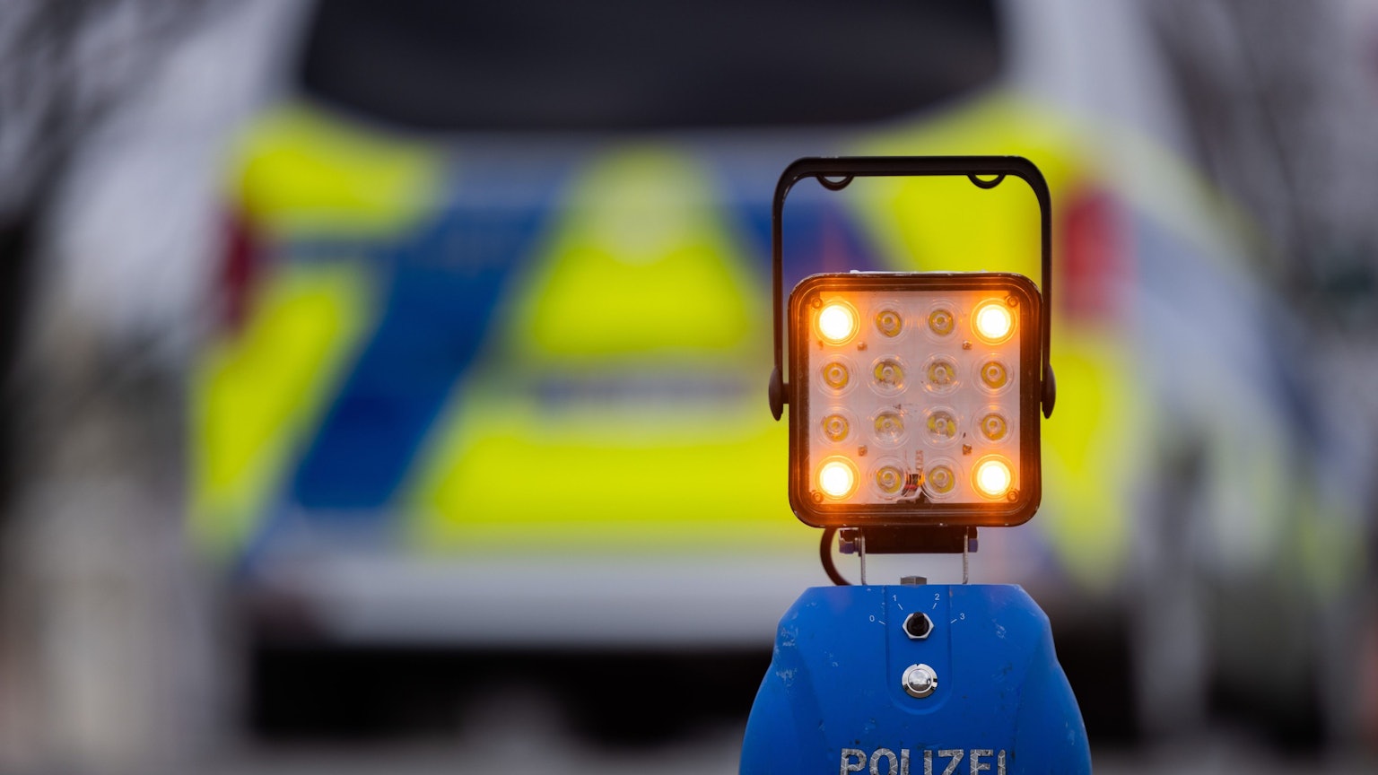 Ein Warnlicht mit der Auschrift „Polizei“ steht auf der Straße vor einem Einsatzfahrzeug der Polizei.