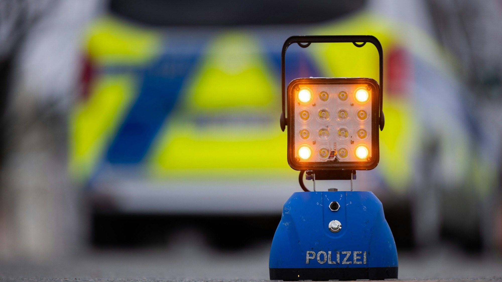Ein Warnlicht mit der Auschrift „Polizei“ steht auf der Straße vor einem Einsatzfahrzeug der Polizei.